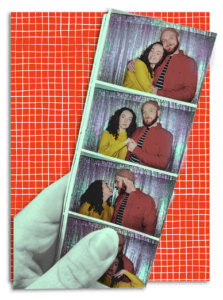 A hand holds up a photobooth strip in which Illustrators Grace Manno and Dashiell Kirk are posed